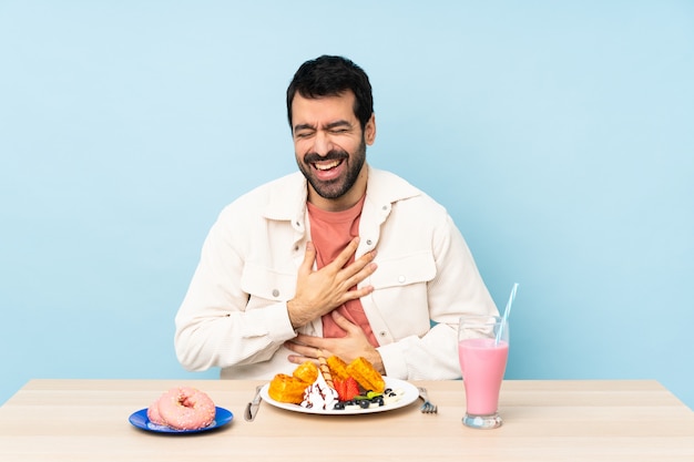 Mężczyzna przy stole ma gofry śniadaniowe i milkshake, uśmiecha się bardzo