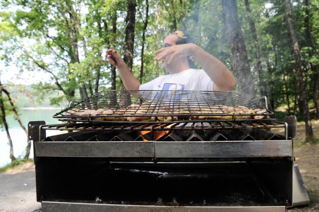 Mężczyzna przygotowuje mięso na grillu w lesie