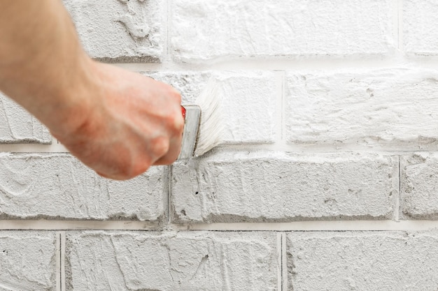 Mężczyzna ręcznie malowany pędzlem biały mur z cegły. Renowacja. Białe tło.