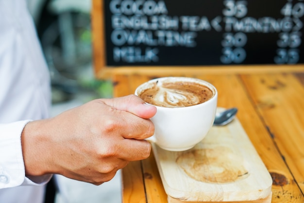 Mężczyzna ręka trzyma kubek kawy latte art.