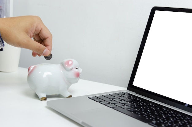 Mężczyzna ręka trzyma monetę w piggy bank finanse i komputer laptop biznesowa koncepcja oszczędzania inwestycji