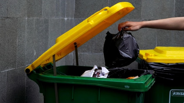 mężczyzna ręka trzyma śmieci czarny worek włożony do kosza. buang sampah pada tempatnya.tempat sampah