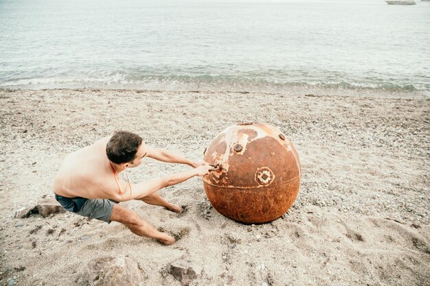 Mężczyzna Robi ćwiczenia Jogi Na świeżym Powietrzu, Stojąc Na Starej Zardzewiałej Pływającej Kopalni Morskiej Na Plaży Z Kamieniami