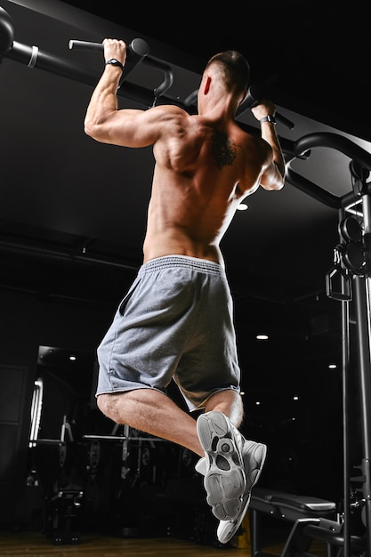 Mężczyzna robi pull-upy na poziomej siłowni, ciemnym tle, pięknym ciele, motywacji Fitness.