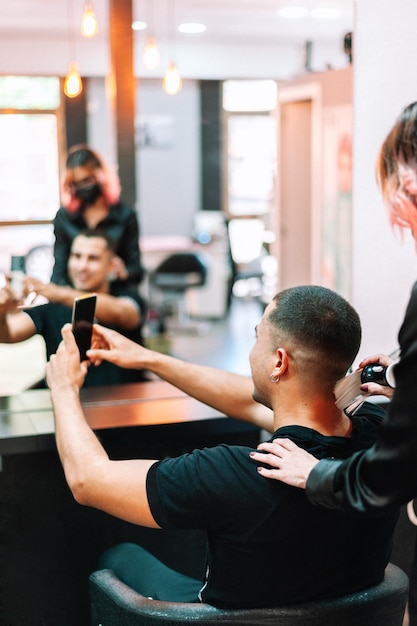 Mężczyzna robi selfie smartfonem w salonie fryzjerskim po obcięciu włosów