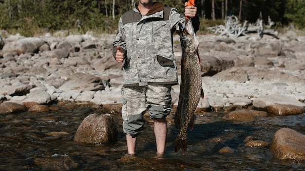 Mężczyzna rybak trzyma dużego szczupaka złowionego na brzegu jeziora