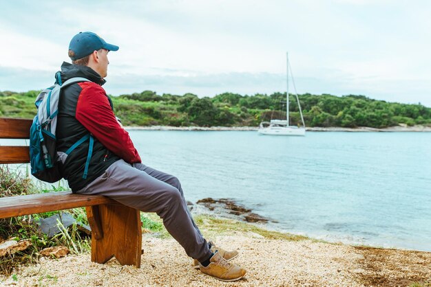 Mężczyzna siedzący na ławce na plaży łodzi na morzu w tle w zatoce