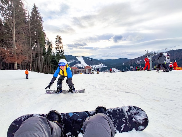 Mężczyzna siedzący na zaśnieżonym wzgórzu ze snowboardową szczęśliwą kobietą przed zimowym ośrodkiem narciarskim