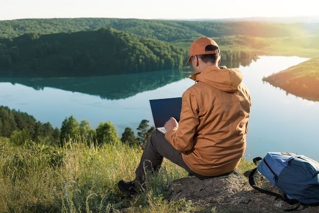 Mężczyzna siedzący samotnie w dzikiej przyrodzie pracuje na laptopie.