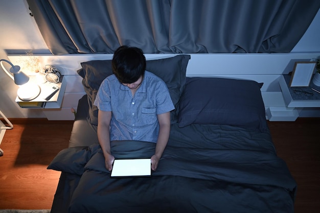 Mężczyzna siedzący w łóżku i korzystający z cyfrowego stołu w nocy