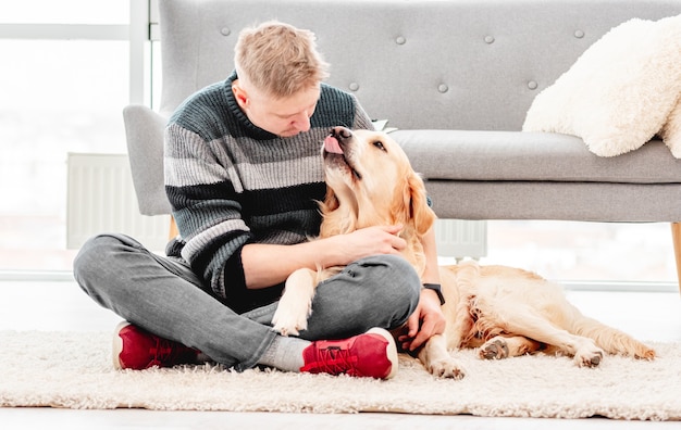 Mężczyzna siedzący z psem golden retriever i przytulanie go na podłodze