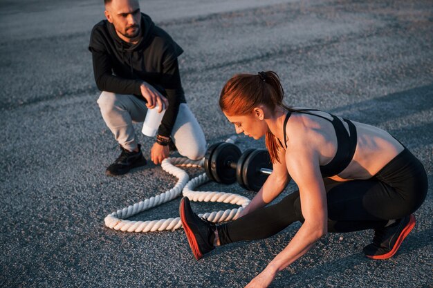 Zdjęcie mężczyzna siedzi i trzyma butelkę wody kobieta i mężczyzna mają dzień fitness na drodze wieczorem razem