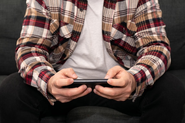 Mężczyzna siedzi na ławce z kraciastą koszulą i telefonem w dłoniach, odtwarzając lub oglądając wideo