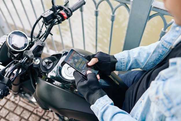 Zdjęcie mężczyzna siedzi na motocyklu i zamawia dostawę jedzenia za pośrednictwem aplikacji na smartfonie