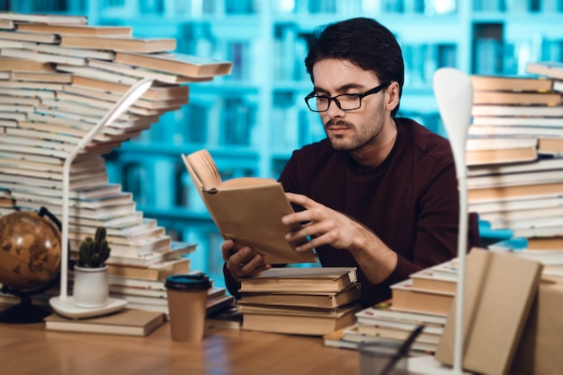 Mężczyzna siedzi przy stole otoczony książkami w bibliotece.