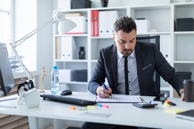 Mężczyzna siedzi w biurze przy stole, trzyma szklankę kawy i długopis w ręku i pracuje z dokumentami