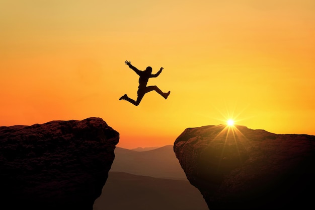 Mężczyzna skacze z klifu na klif nad przepaścią o zachodzie słońca, kreatywny pomysł. Koncepcja sukcesu i ryzyka