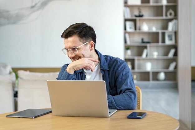 Mężczyzna skupiający się na kontemplacji podczas pracy z laptopem i tabletem w stylowo umeblowanym domu