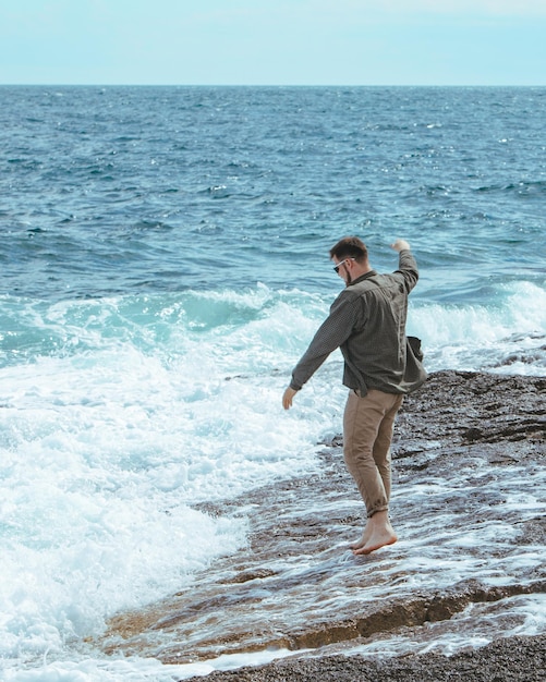 Mężczyzna spacerujący po kamienistej plaży w wietrzny dzień letnie wakacje cieszyć się widokiem na morze