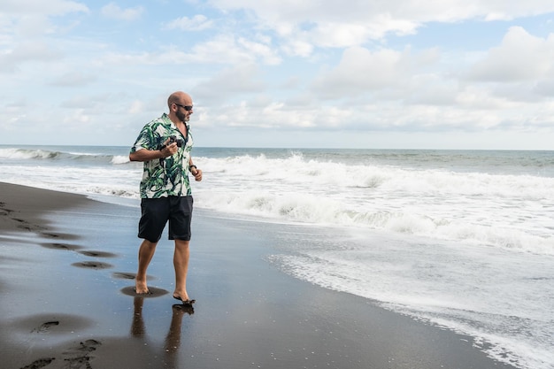 Mężczyzna spacerujący wzdłuż tropikalnej plaży z aparatem