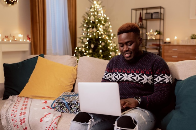 Mężczyzna Spędza Wieczór Po Pracy W Przytulnym, Ciepłym Domu Ze świąteczną Atmosferą Trzyma Laptopa