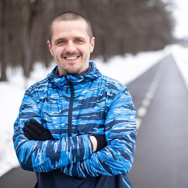 Mężczyzna sportowiec biegacz patrzący w kamerę i uśmiechający się stojąc na bieżni w zimie