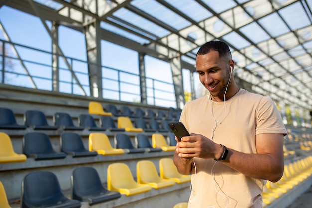 Mężczyzna sportowiec używa aplikacji na telefonie po zajęciach fitness na stadionie trener w słuchawkach używa smartfona