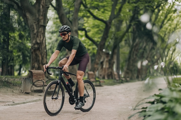 Mężczyzna sportowiec w odzieży sportowej na rowerze wzdłuż parku miejskiego