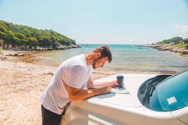 Mężczyzna sprawdza na mapie w miejscu przeznaczenia maski samochodu plaża morska na tle