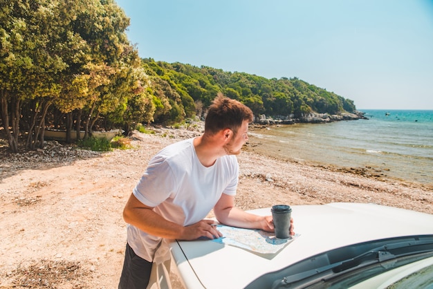 Mężczyzna sprawdza na mapie w miejscu przeznaczenia maski samochodu plaża morze na tle czasu letniego