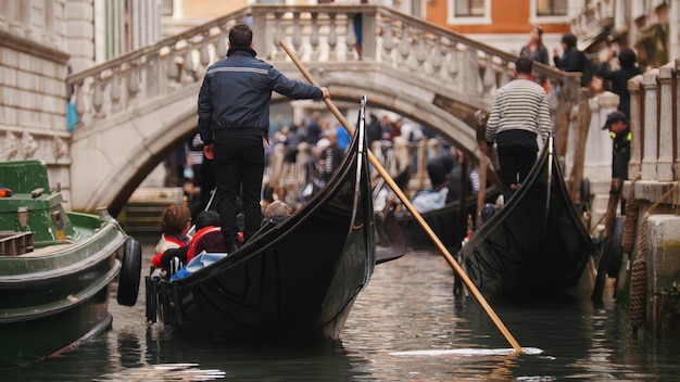 Zdjęcie mężczyzna stoi na łodzi z ludźmi trzymającymi w ręku wiosło podróż po kanałach weneckich