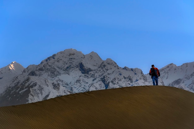Mężczyzna stoi na wydmie z górą w tle.
