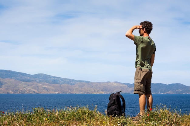 Zdjęcie mężczyzna stoi na wzgórzu i patrzy na morze, a niebo jest niebieskie.
