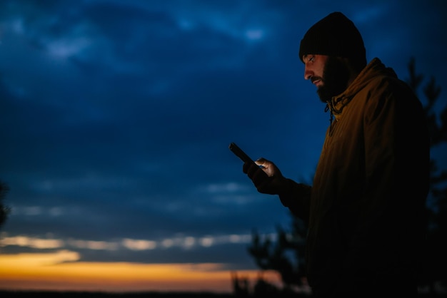 Mężczyzna stoi z telefonem na tle nocnego nieba Wędrowiec po górach o zachodzie słońca