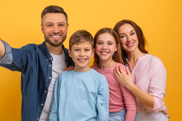 Mężczyzna stoi ze swoją rodziną, robiąc selfie za pomocą smartfonu, uśmiechają się i pozują