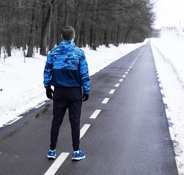 Zdjęcie mężczyzna stojący na bieżni i patrzący na nią przed porannym biegiem zimą