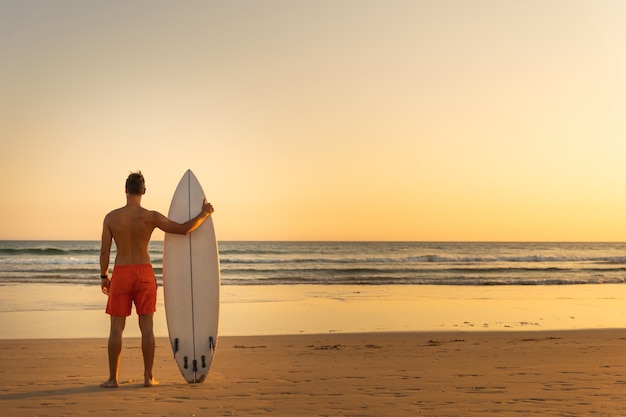 Mężczyzna stojący na brzegu, trzymający widok z tyłu na deskę surfingową