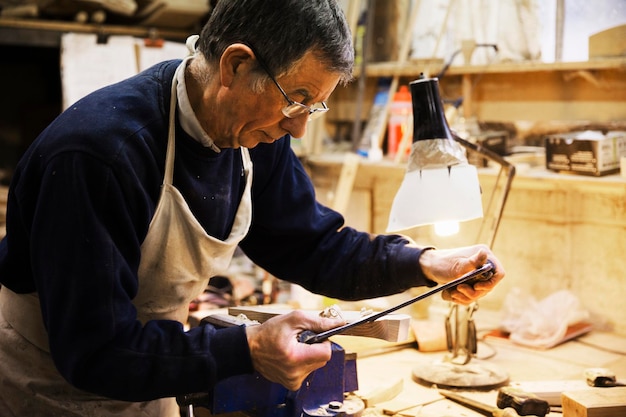 Mężczyzna stojący przy stole warsztatowym w warsztacie stolarskim, pracujący na kawałku drewna zabezpieczonym w imadle stołowym
