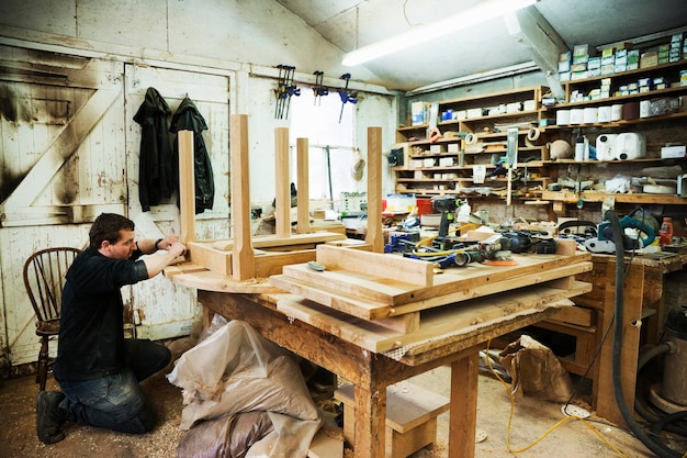 Mężczyzna stojący w warsztacie stolarskim pracujący na listwie drewnianego stołu