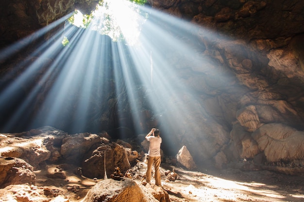 Mężczyzna stojący z aparatem Aby zrobić zdjęcie w jaskini rano o wschodzie słońca