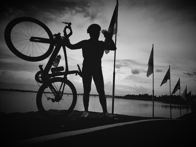 Mężczyzna stojący z rowerem przy fladze przy drodze nad jeziorem