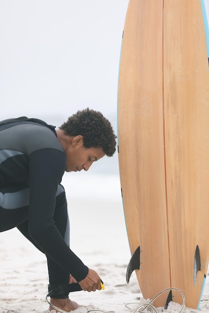 Zdjęcie mężczyzna surfer wiąże smycz na desce surfingowej na nodze na plaży