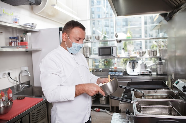 Mężczyzna szef kuchni noszący maskę medyczną podczas pracy w kuchni restauracji, kopia przestrzeń