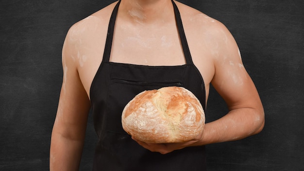 Zdjęcie mężczyzna szef kuchni z chlebem w ręku na czarnym tle koncepcja gotowania