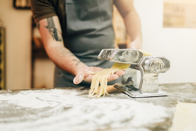 Zdjęcie mężczyzna szefa kuchni w fartuch gotuje świeże domowe fettuccine w maszynie do makaronu na drewnianym stole w kuchni