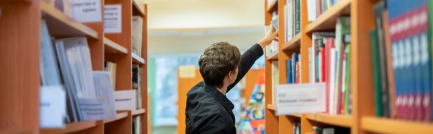 mężczyzna szukający książki w bibliotece uniwersyteckiej poziomy szeroki baner b