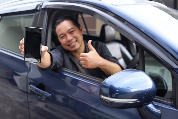 Mężczyzna taksówkarz online pokazujący ekran telefonu i kciuk do góry, siedząc w samochodzie