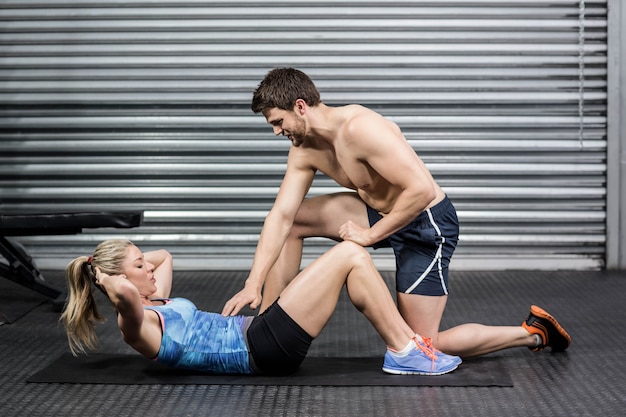 Mężczyzna trener pomaga kobieta z siedzieć ups w siłowni crossfit