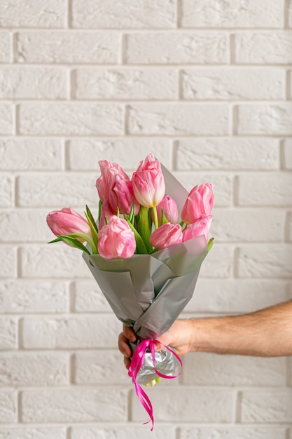 Zdjęcie mężczyzna trzyma bukiet pięknych różowych wiosennych tulipanów w pobliżu białego ceglanego muru.
