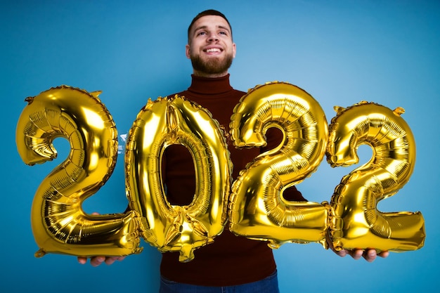 Mężczyzna trzyma cyfry 2022 ze złotych balonów. Nadchodzący nowy rok. Selektywne skupienie się na piłkach